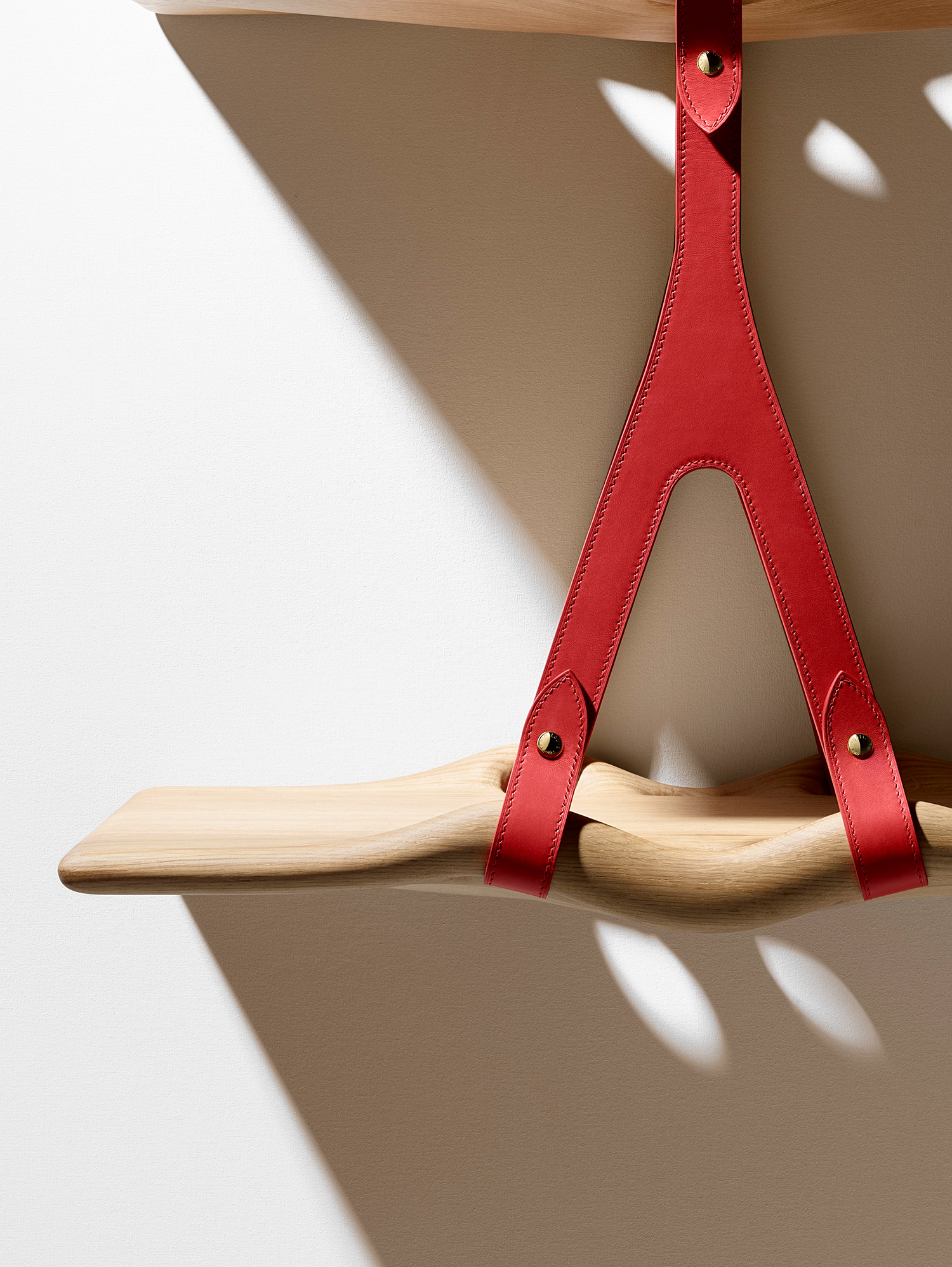A detail of the Swell Waves Shelf, crafted of smoothly polished oak with leather straps as brackets.