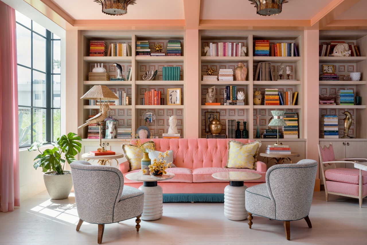 The Wes Anderson-inspired library lounge features a tufted pink velvet sofa trimmed with turquoise fringe